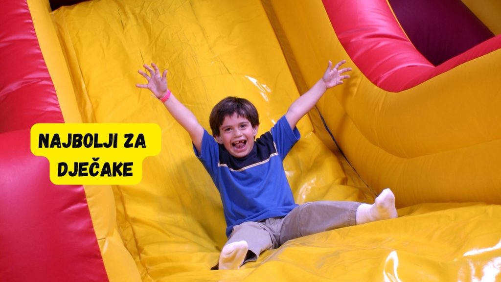 Child joyfully sliding down colorful inflatable slide, arms raised, with text overlay Najbolji za dječake in bold letters.